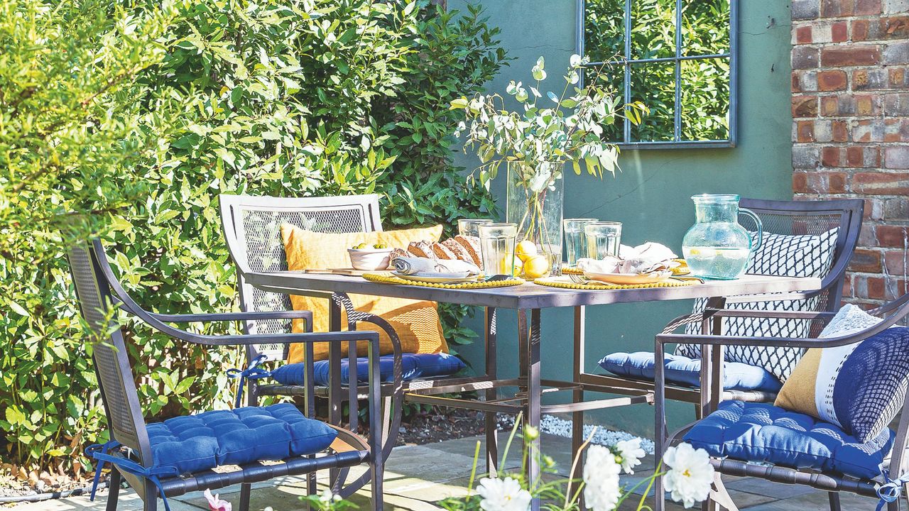 Garden mirror on blue wall next to outdoor seating area with blue cushions