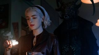 Kiernan Shipka as Sabrina Spellman holding a candle with a demon behind her during the Netflix show, Chilling Adventures of Sabrina.