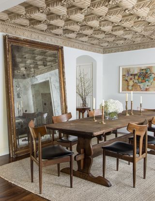 Dining room with wood table and chairs, large mirror propped against wall, and ornate ceiling