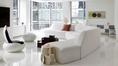 Image of an all-white living room that is design in a space-age aesthetic. There is a curved white sofa, two white egg chairs with black interiors, and a black geometric coffee table between the sofa and chairs. 