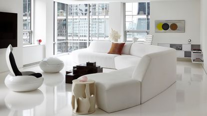 Image of an all-white living room that is design in a space-age aesthetic. There is a curved white sofa, two white egg chairs with black interiors, and a black geometric coffee table between the sofa and chairs. 