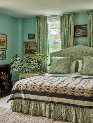 A traditionally decorated room features vibrant aquamarine walls, green curtains and bedding, fresh flowers, and plenty of framed artworks hanging across it.