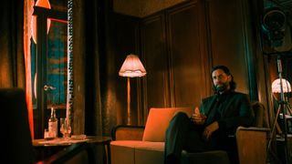 Photo of Ilkka Villi on the live action Alan Wake 2 Hotel Set posing with a glass of whisky in character as Alan wake