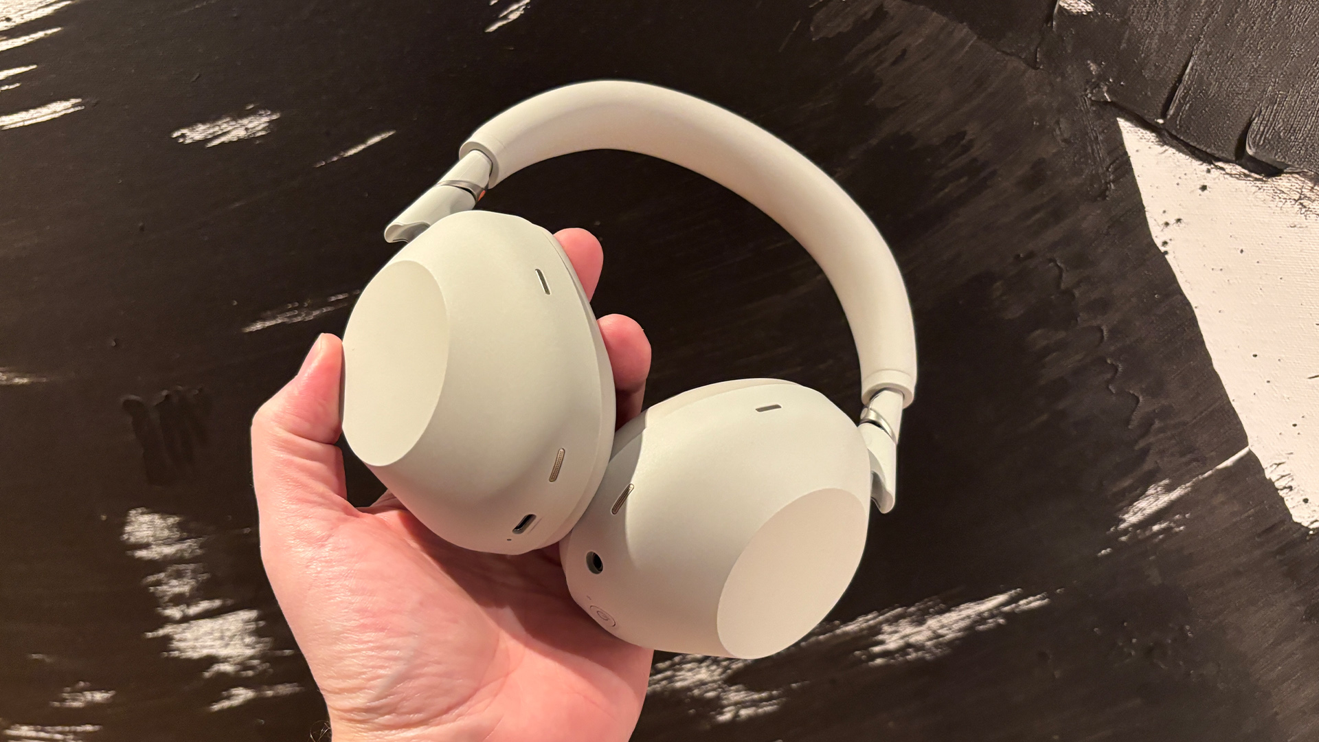 Sony WH-1000XM6 over-ear headphones being held in someone's hand with a black painting in the background