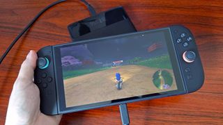 Hand holding Switch 2 with Mario Kart World gameplay on screen with Baseus Blade power bank charging handheld.
