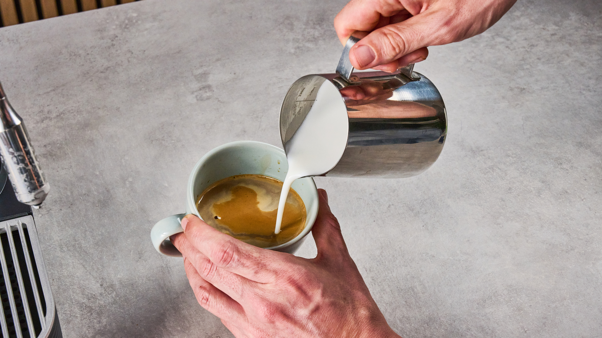 A man pours foamed milk into a double espresso.