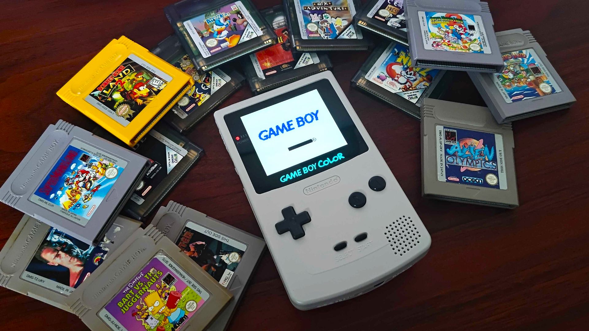 Game Boy Color AMOLED modded console next to cartridges on woodgrain table