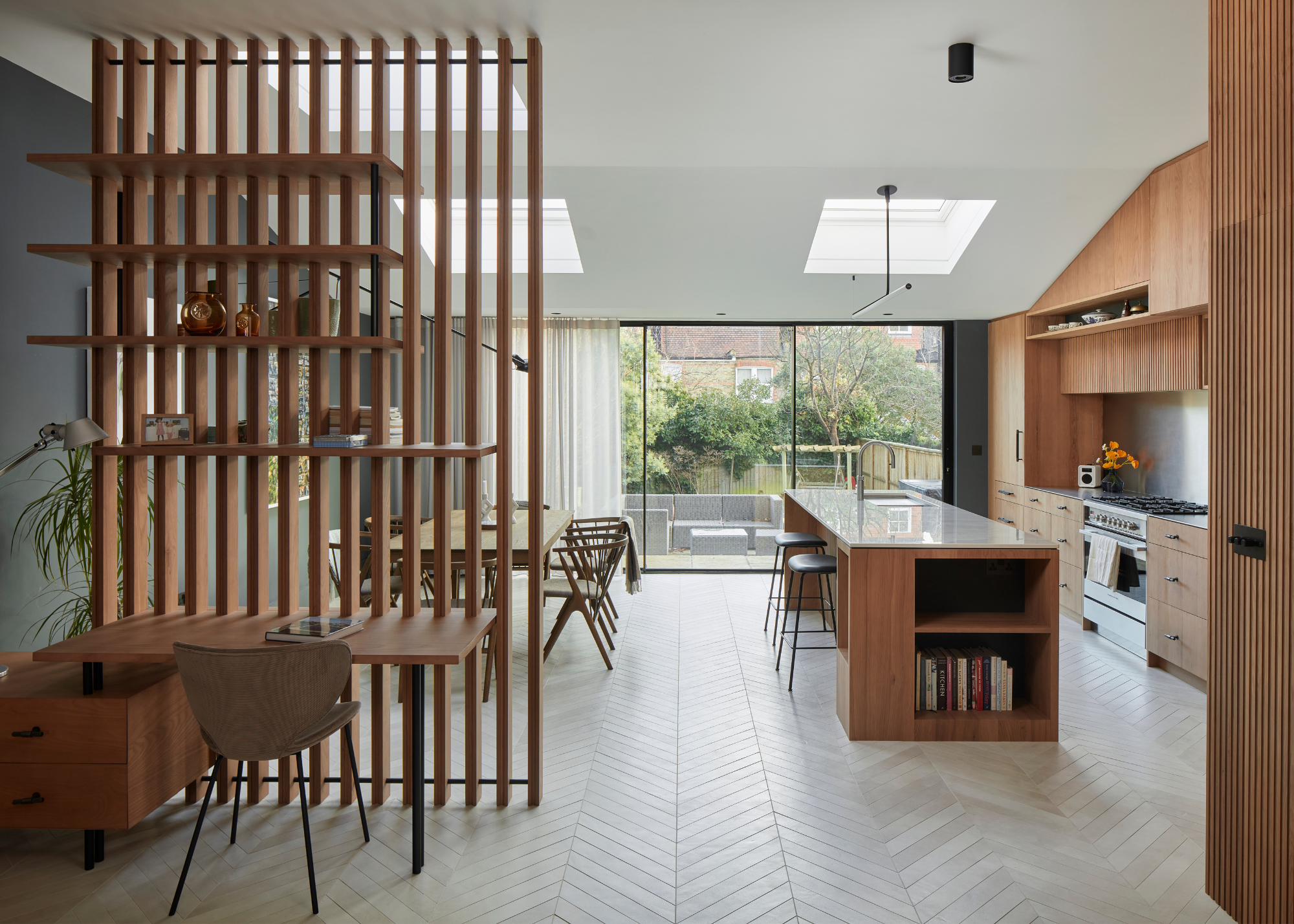 A spacious light modern wood panelled kitchen with a wooden room divider of vertical slats