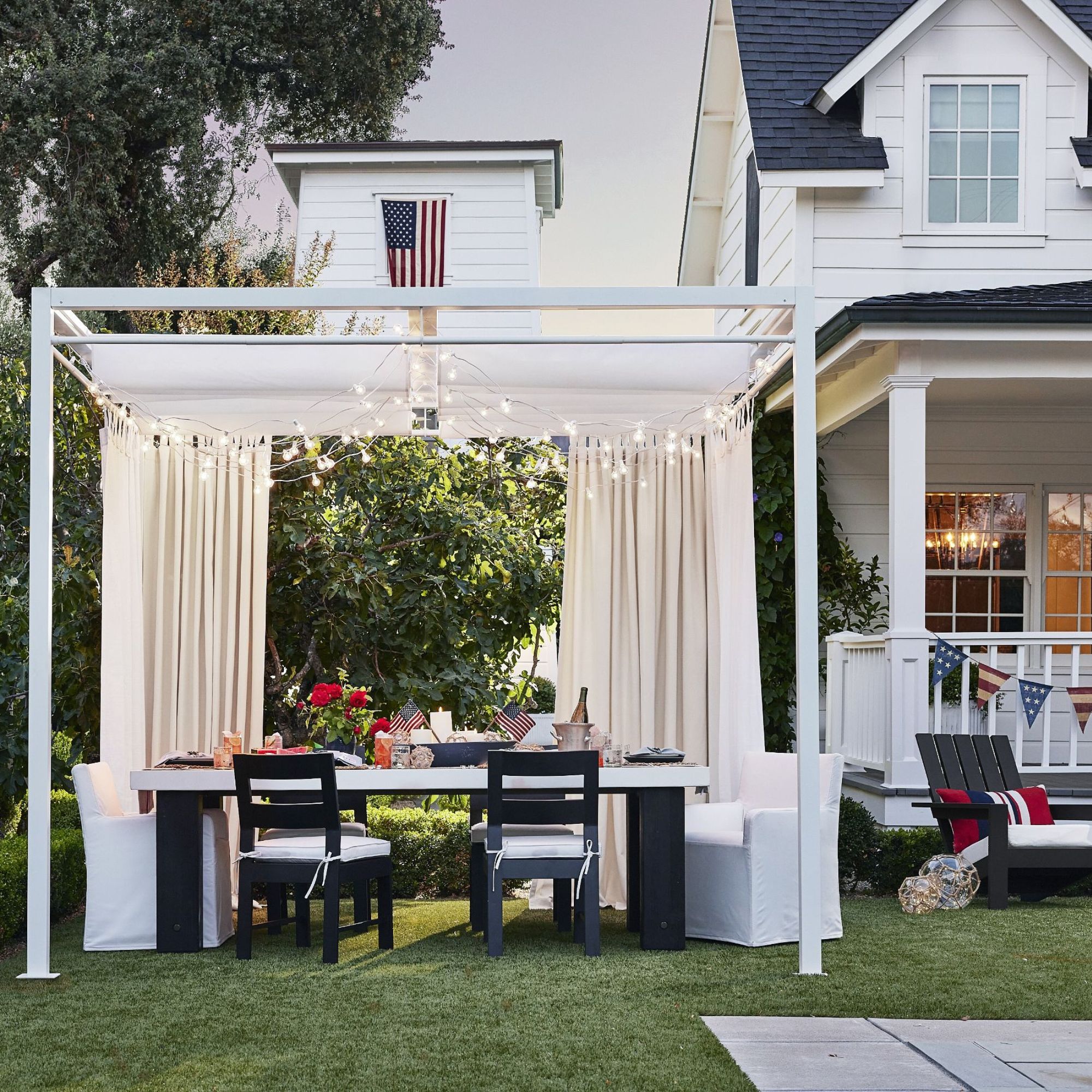 Back yard with a white gazebo with cream curtains and a table set up for outdoor dining