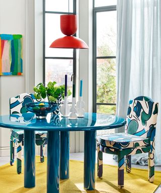 dining room with colourful round table, upholstered chairs in a playful pattern and bright rug