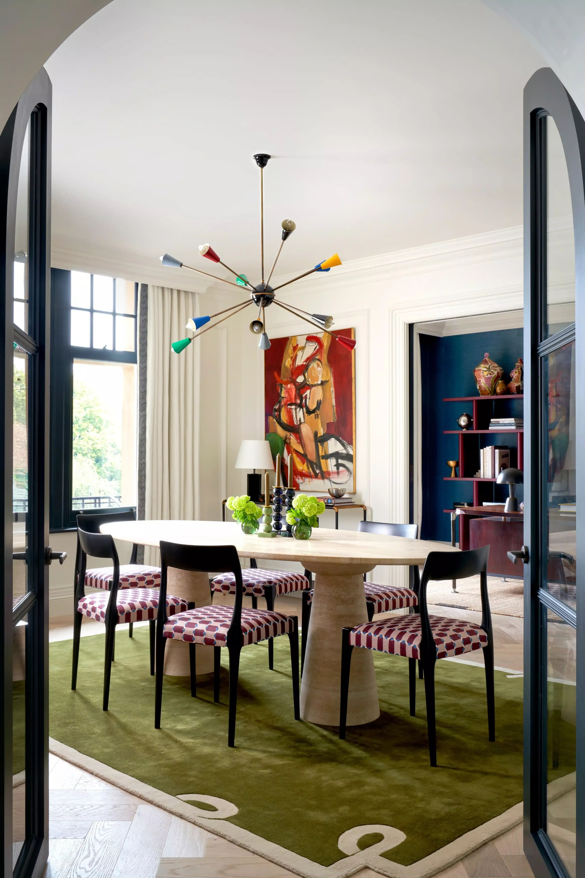 mid-century modern style dining room with sputnik light, green rug, patterned chairs, a travertine dining table, and artwork on the wall