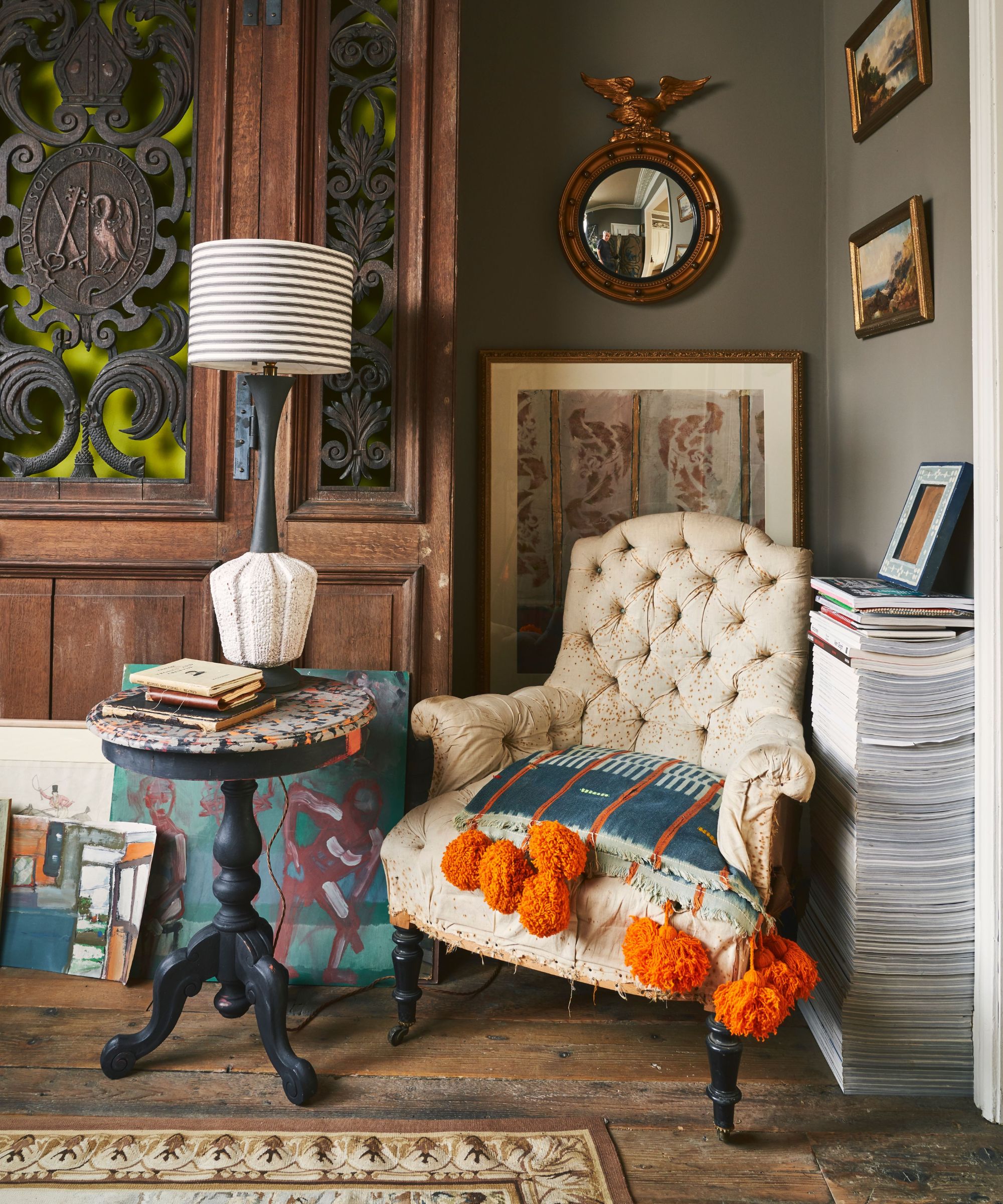 A characterful corner featuring a vintage tufted armchair with a bold cushion trimmed in bright orange pompoms.