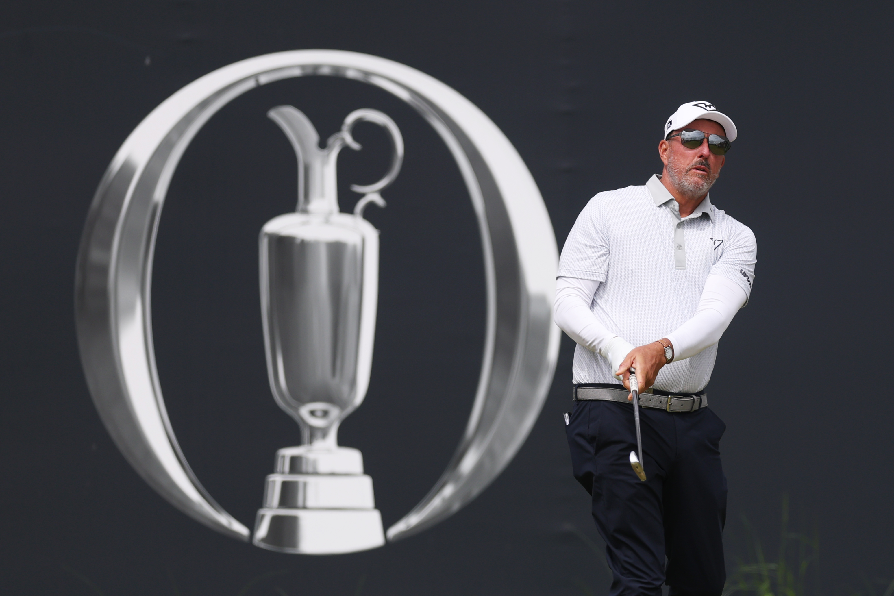 Phil Mickelson hits a shot in front of an Open Championship banner