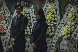 a man and a woman stand in front of floral arrangements at a funeral
