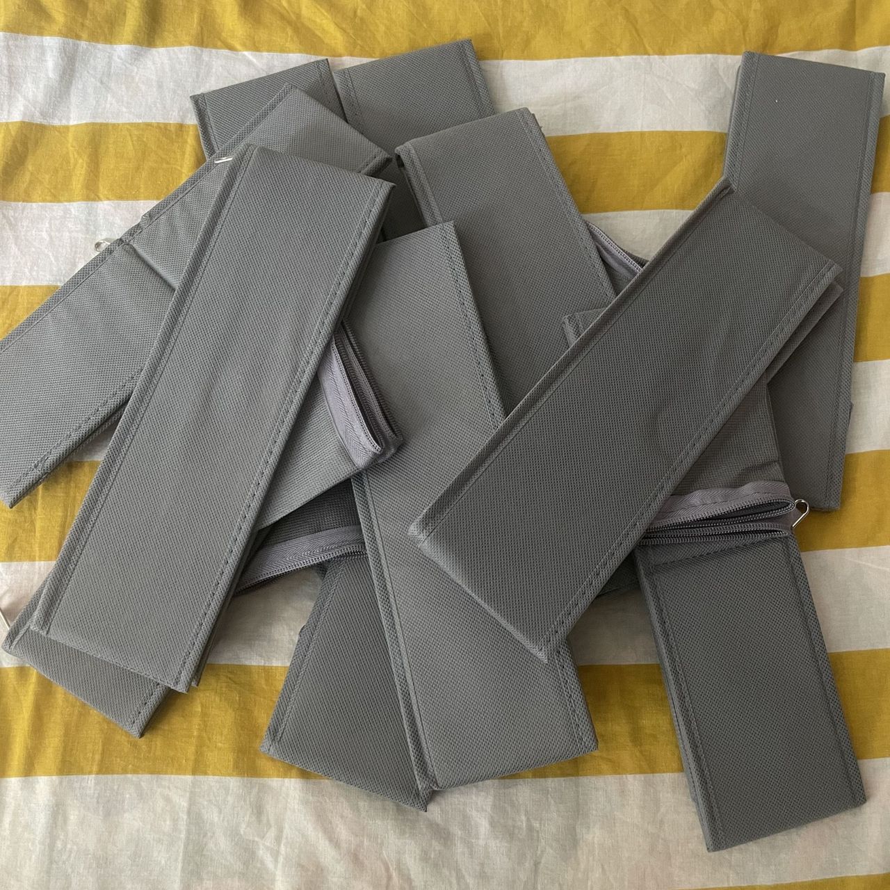 Folded grey clothes organisers in a pile on white and yellow bedding