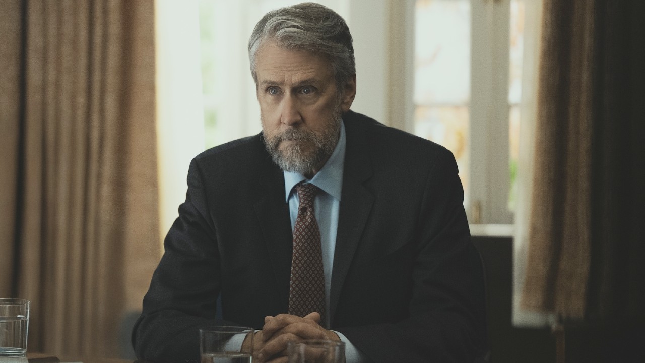 Alan Ruck as Dean Riggs in Rooster sitting at a desk.