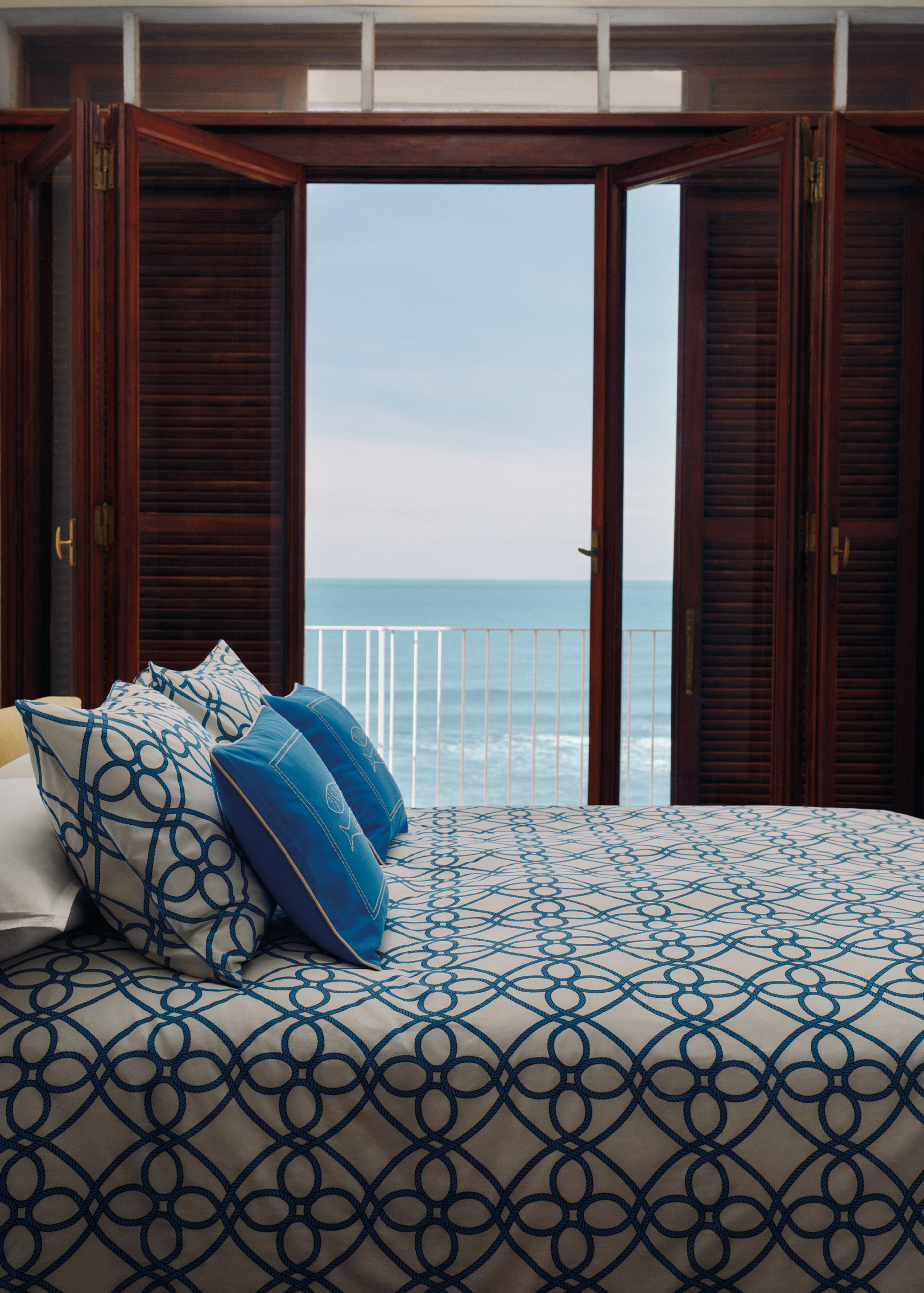 A bedroom with slatted doors leading to a balcony. Also pictured is a bed in bright blue and white patterned bedding