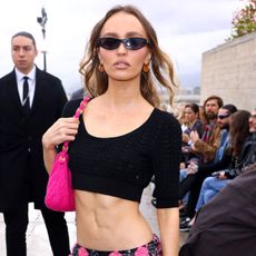 Lily-Rose Depp wears a black crop top with a pink shoulder bag