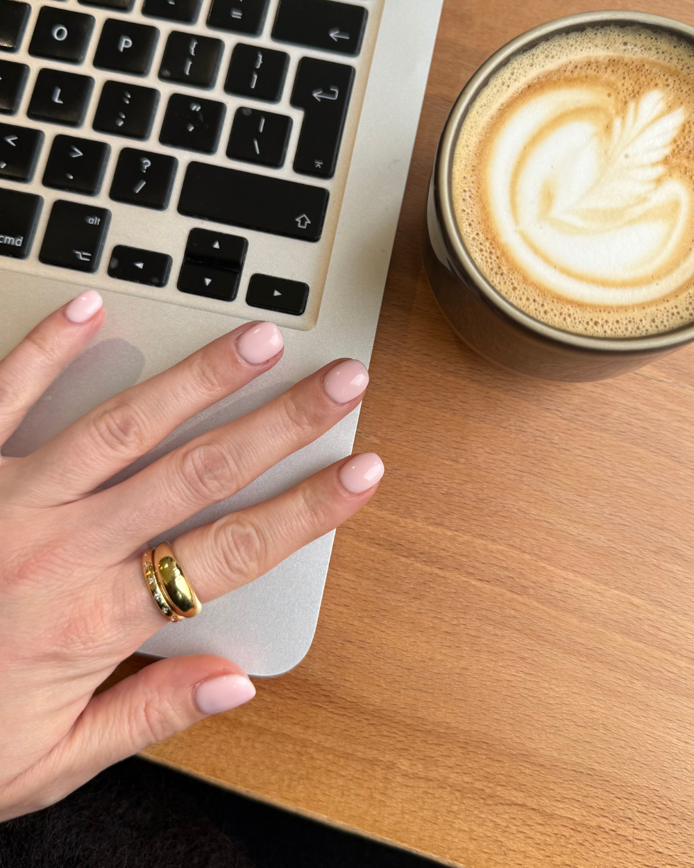 Bird&#039;s eye view of Lucy&#039;s nails with Hard BIAB in the shade 19, over a laptop and wooden table with a cup of coffee