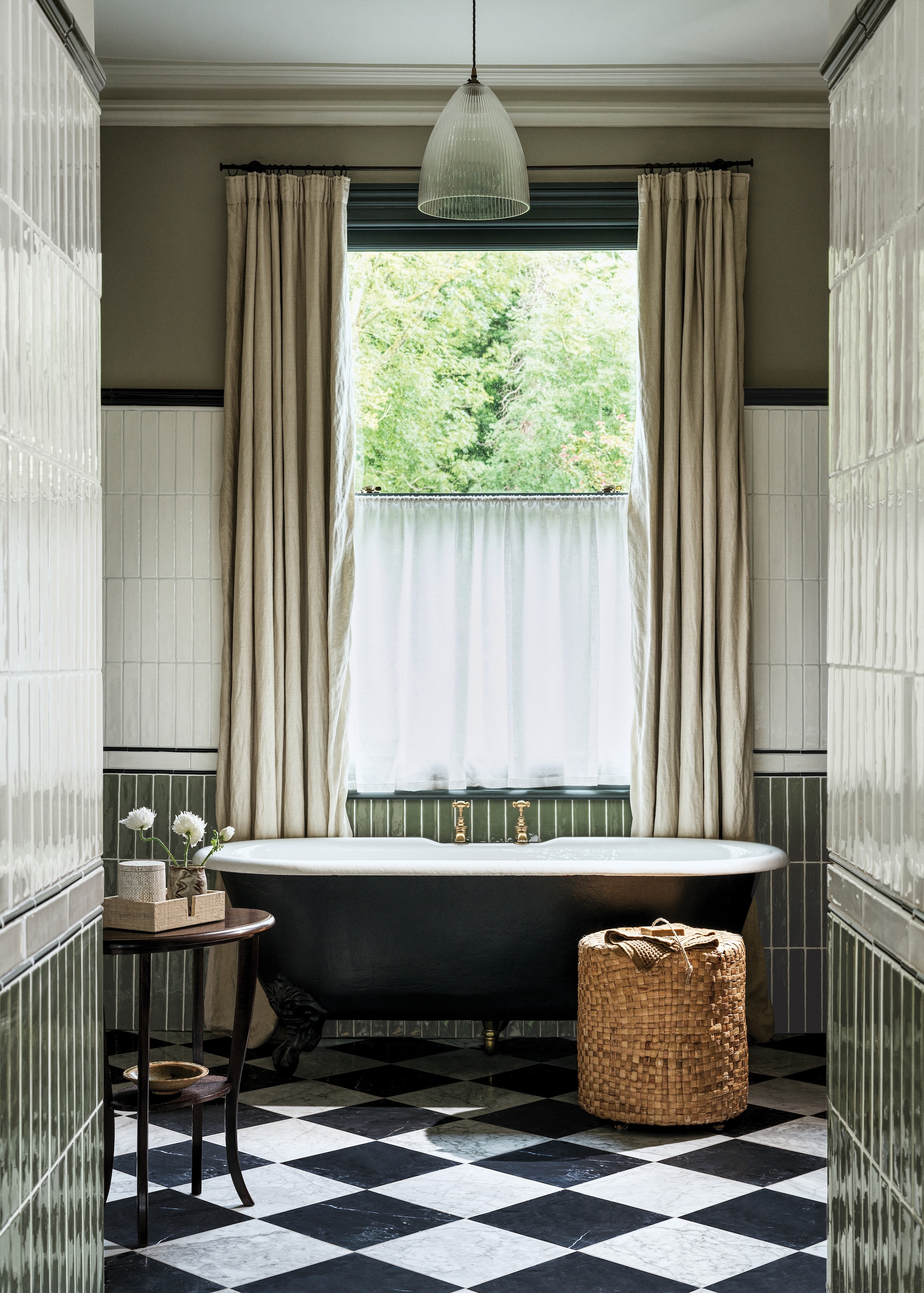 A classic green and neutral bathroom scheme with a rolltop bath and brass taps, linen curtains and a checkerboard floor