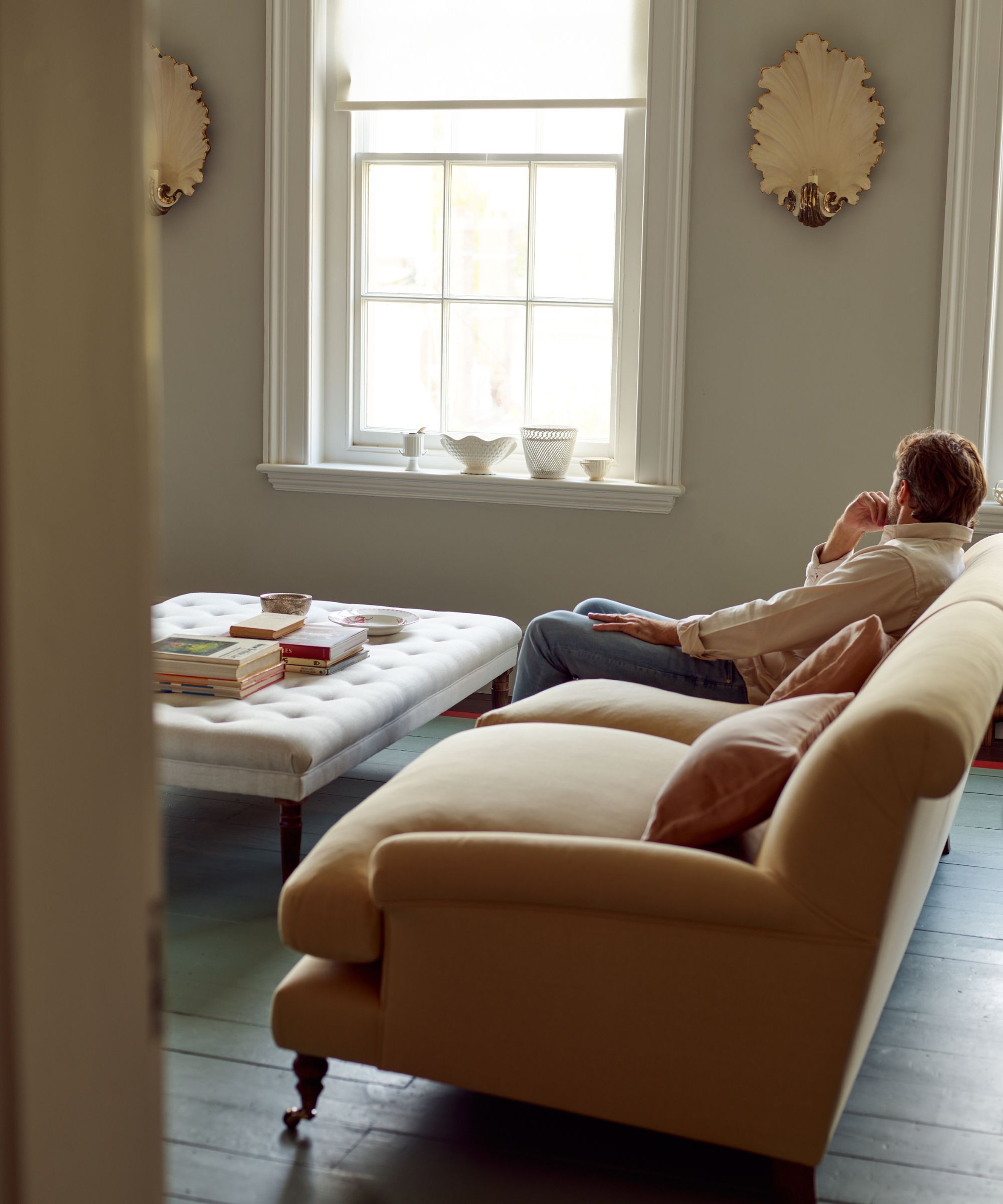 Room with large straw yellow sofa, grey walls and brass wall lights