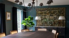 dining room with teal blue walls, antique tapestry, oval wooden dining table, dark brown console, chandelier and dark blue velvet curtains