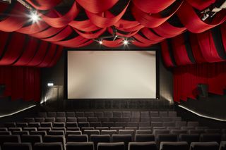 Interior view of a screen at Pálás Cinema featuring a large screen, rows of dark coloured seats, lighting and a ceiling with red fabric draping which continues down the side walls