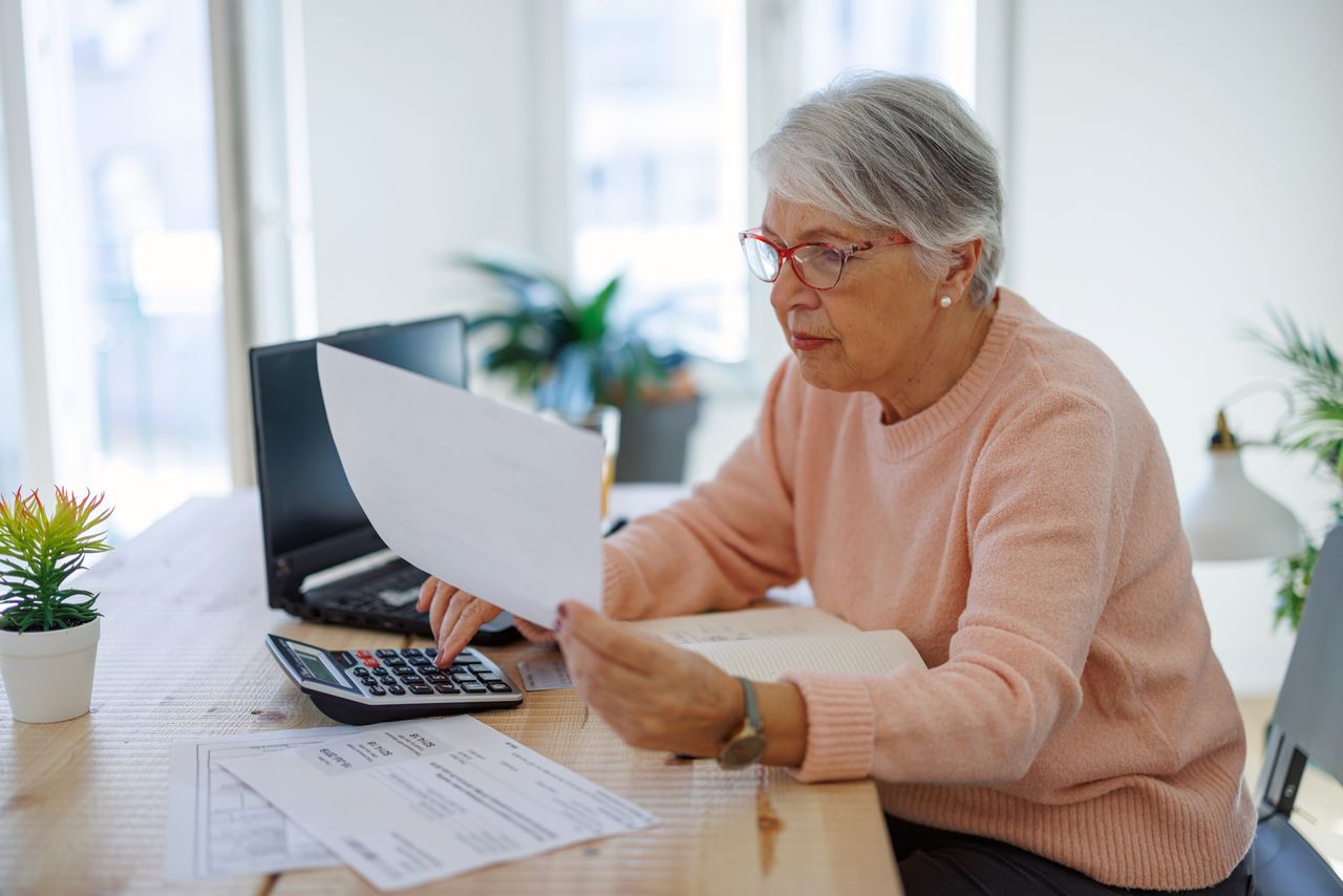 Pensive older woman using laptop paying bills online at home