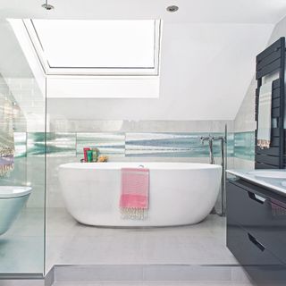 en suite bathroom installation in loft light grey floor tiles freestanding tub, black double vanity unit and black towel radiator