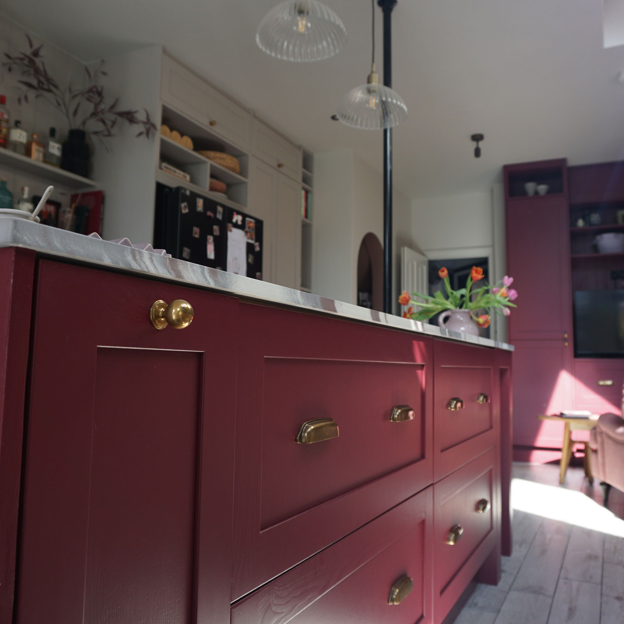 Close up of burgundy kitchen drawers on marble topped island with brass pull