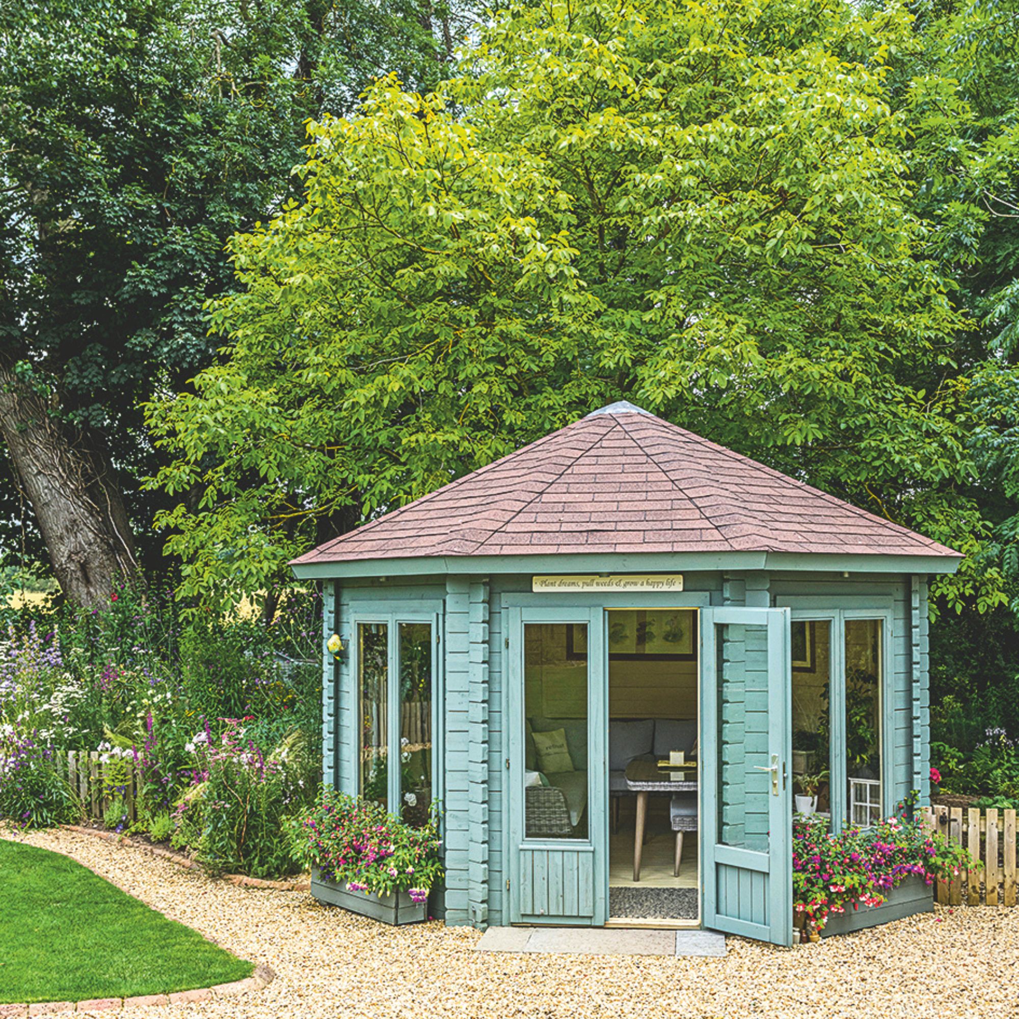 garden shed on pebbled ground framed with plant border and greenert
