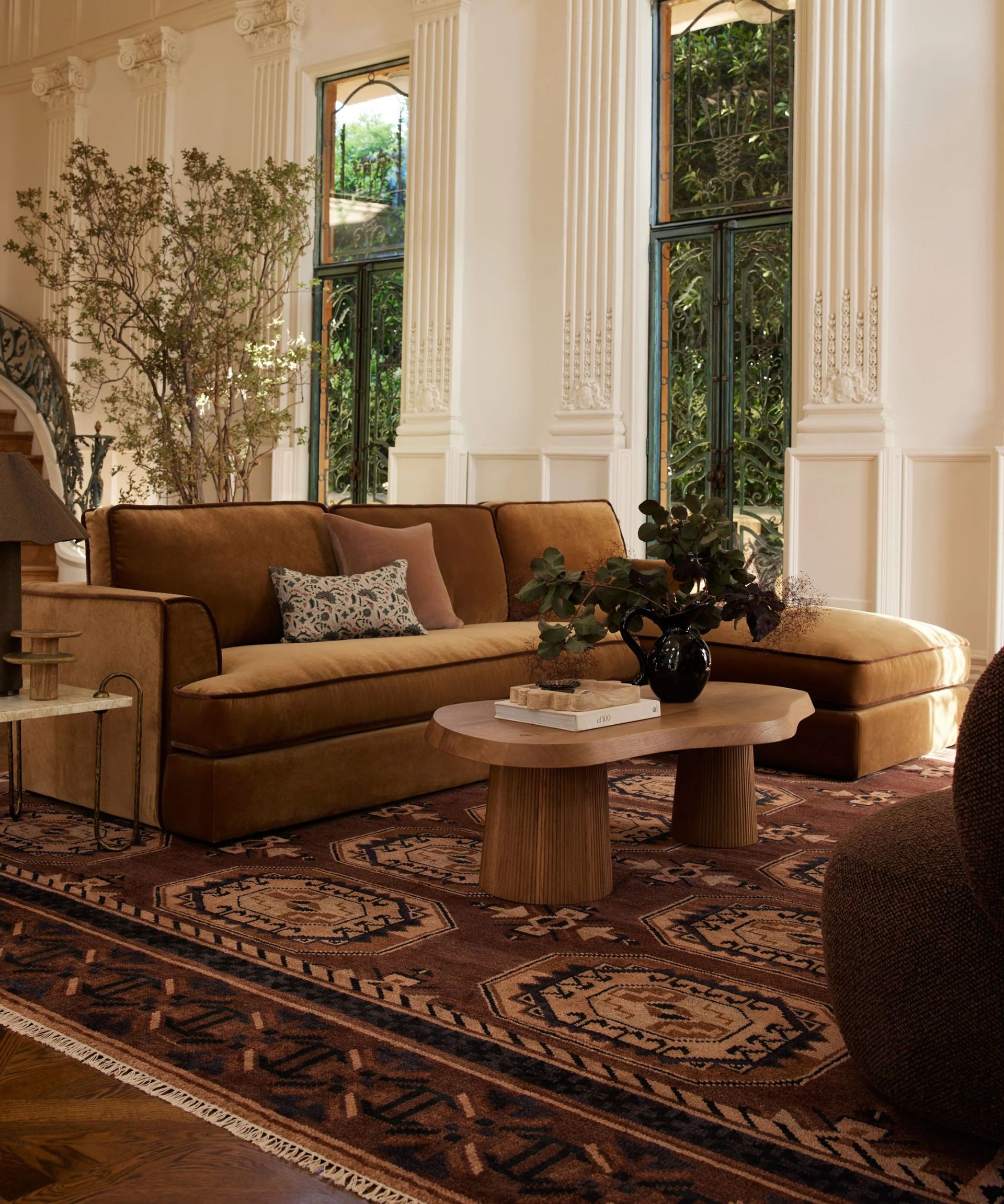 Living room with woven Persian style rug, velvet large sofa, wood coffee table, large plants