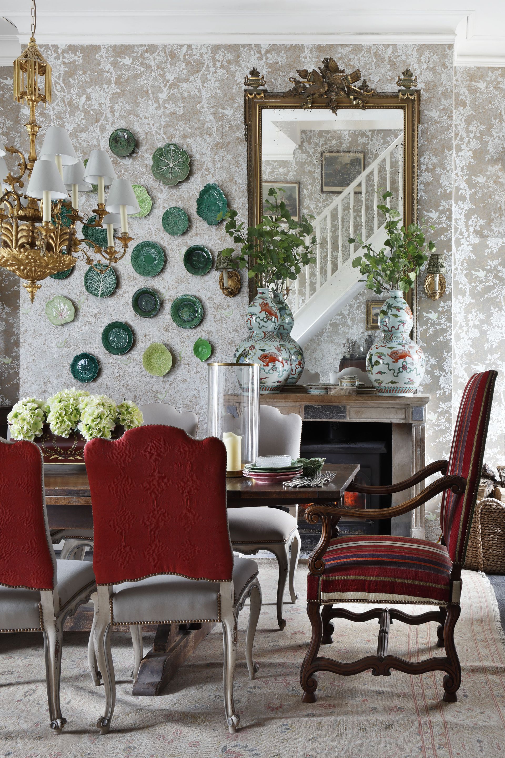 damask style wallaper in dining room with table setting, ornate mirror, plates on the wall, gold chandelier, upholstered dining chairs