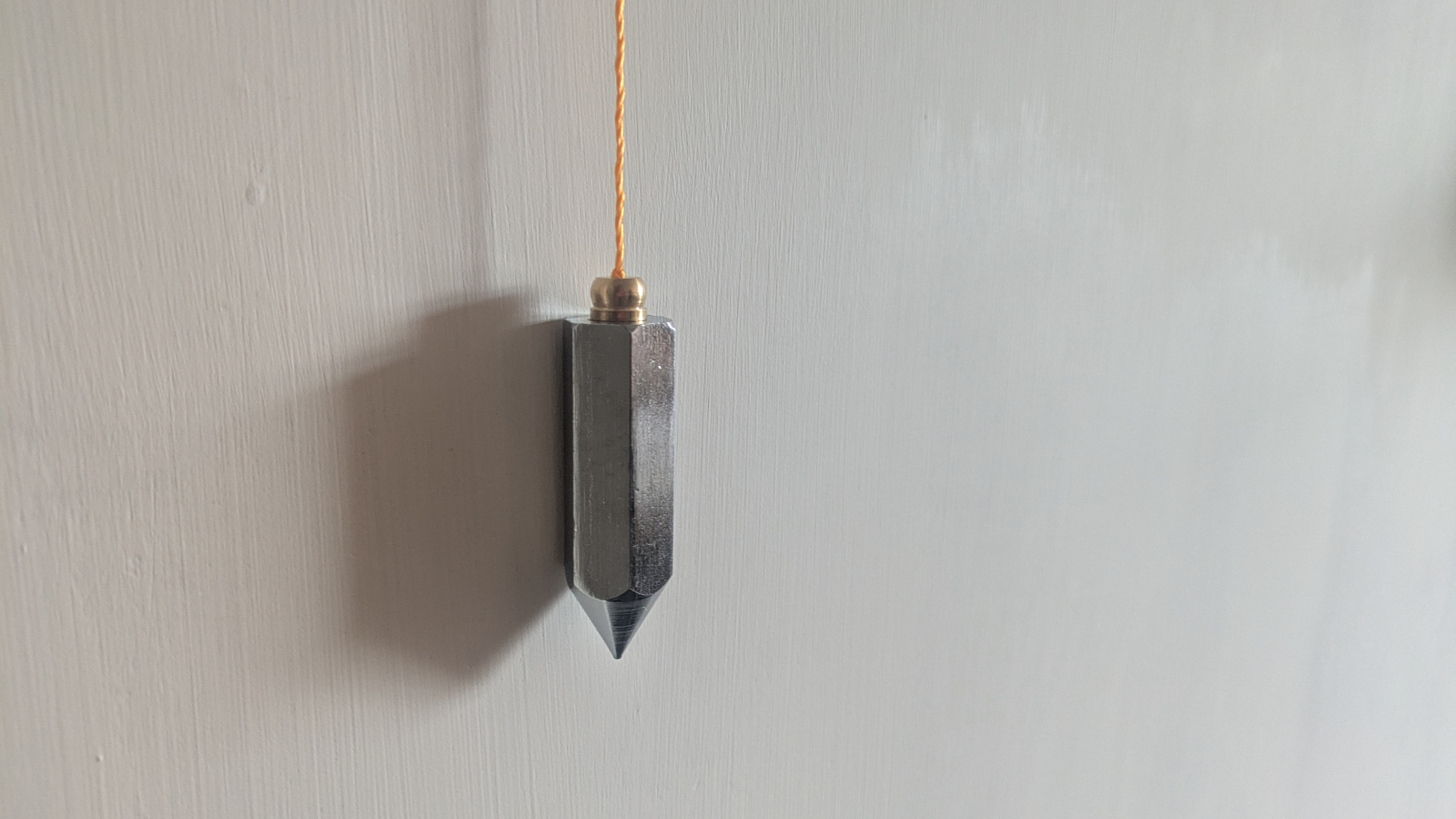 A plumb bob suspended on a line against a wall