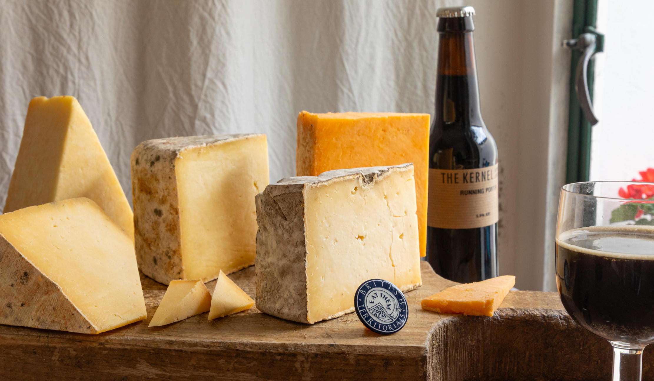 Five cheeses stand on a chopping board, with a bottle of beer