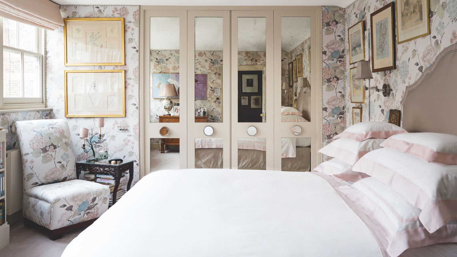 Small bedroom with mirrored four-door built-in closet, white bedding, small chair with side table and floral pastel wallpaper