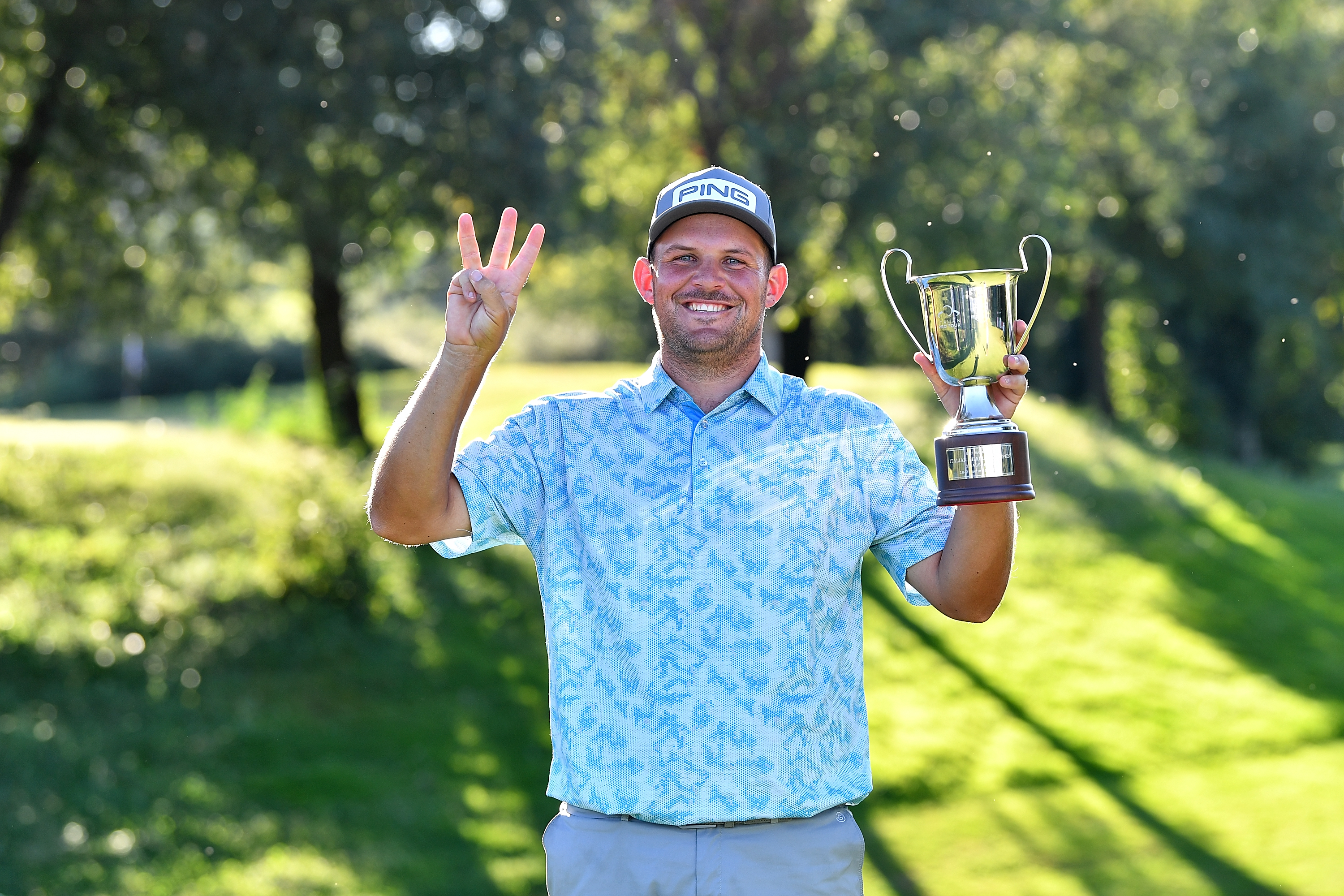 JC Ritchie holds a trophy holding three fingers in the air