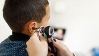 Doctor checking little boy's ears with an otoscope 