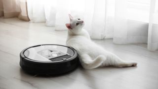 A white cat laying on the floor next to a robot vacuum cleaner
