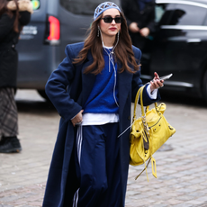 fashion week attendee wearing blue headcap, sweater, track pants, yellow purse