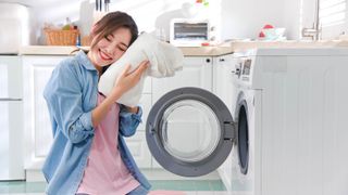 A woman holding a towel to her face in front of a washing machine