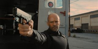Jason Statham aims his gun in front of the truck in Wrath of Man.
