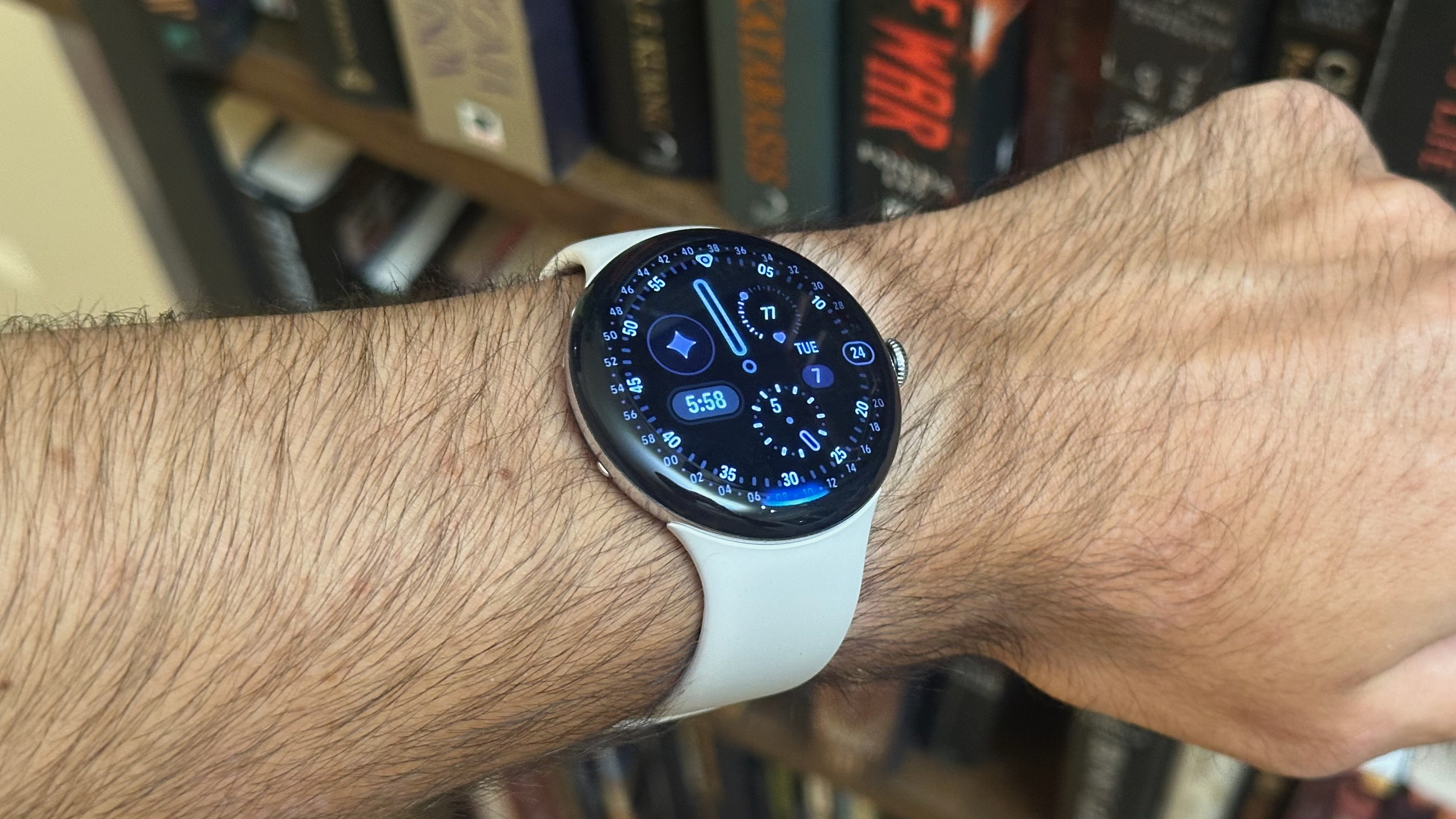 The Google Pixel Watch 4 with the Corsa watch face on the author's wrist, with a blue line along the bottom edge signaling that Gemini Raise to Talk is active.