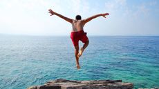A man jumps from a rock ledge into the ocean.