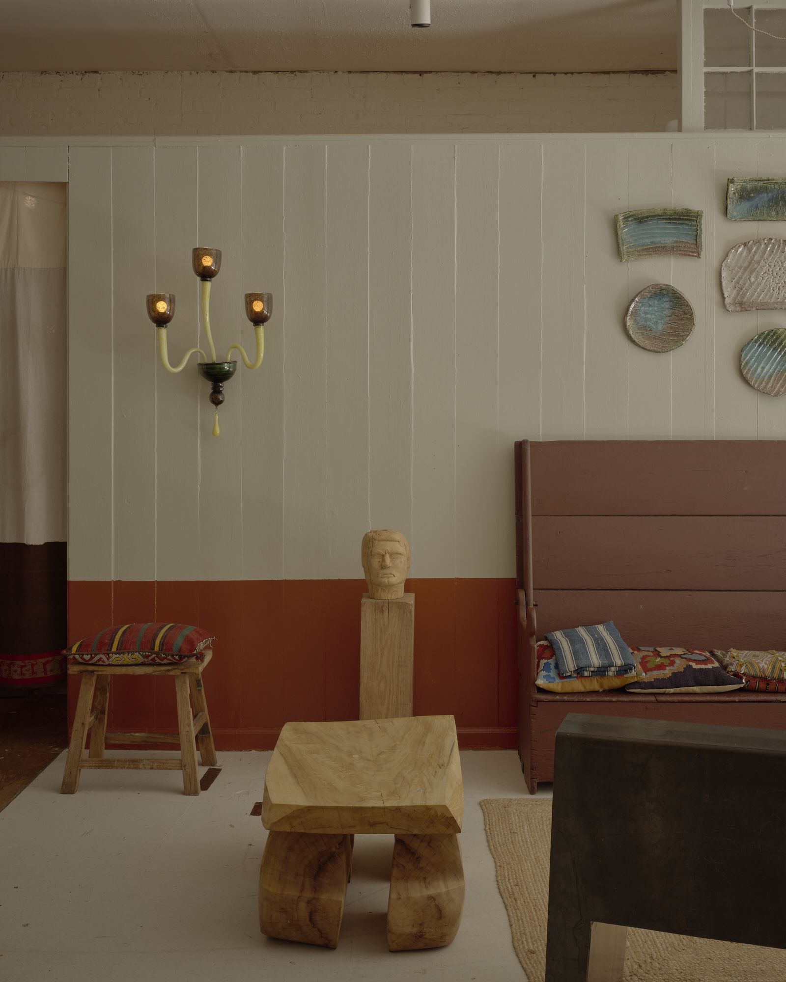 A gallery-like home filled with quirky sculptures in pastel tones, white-washed and cream-painted walls, and organic shaped furniture, including chairs, stools, and coffee tables, along with artworks.