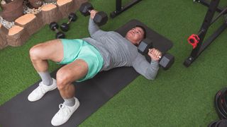 Man performs dumbbell floor press with glute bridge hold
