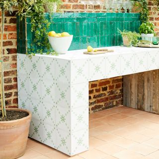 outdoor kitchen with decorative tiled prep area in green and white, lemons, chopping boards with herbs