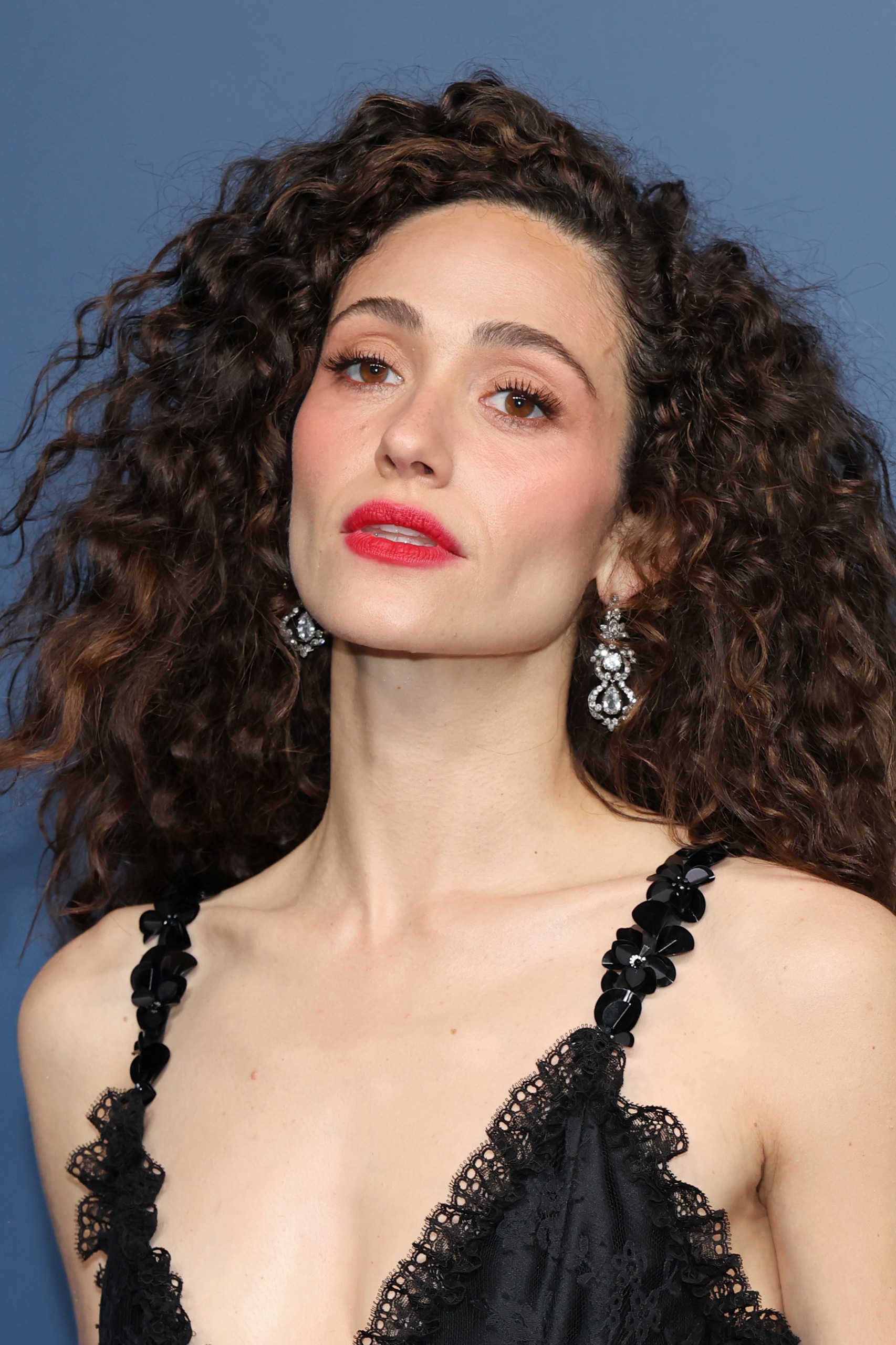 Emmy Rossum with voluminous curly hair, red lipstick and blush at the 2026 Emmys
