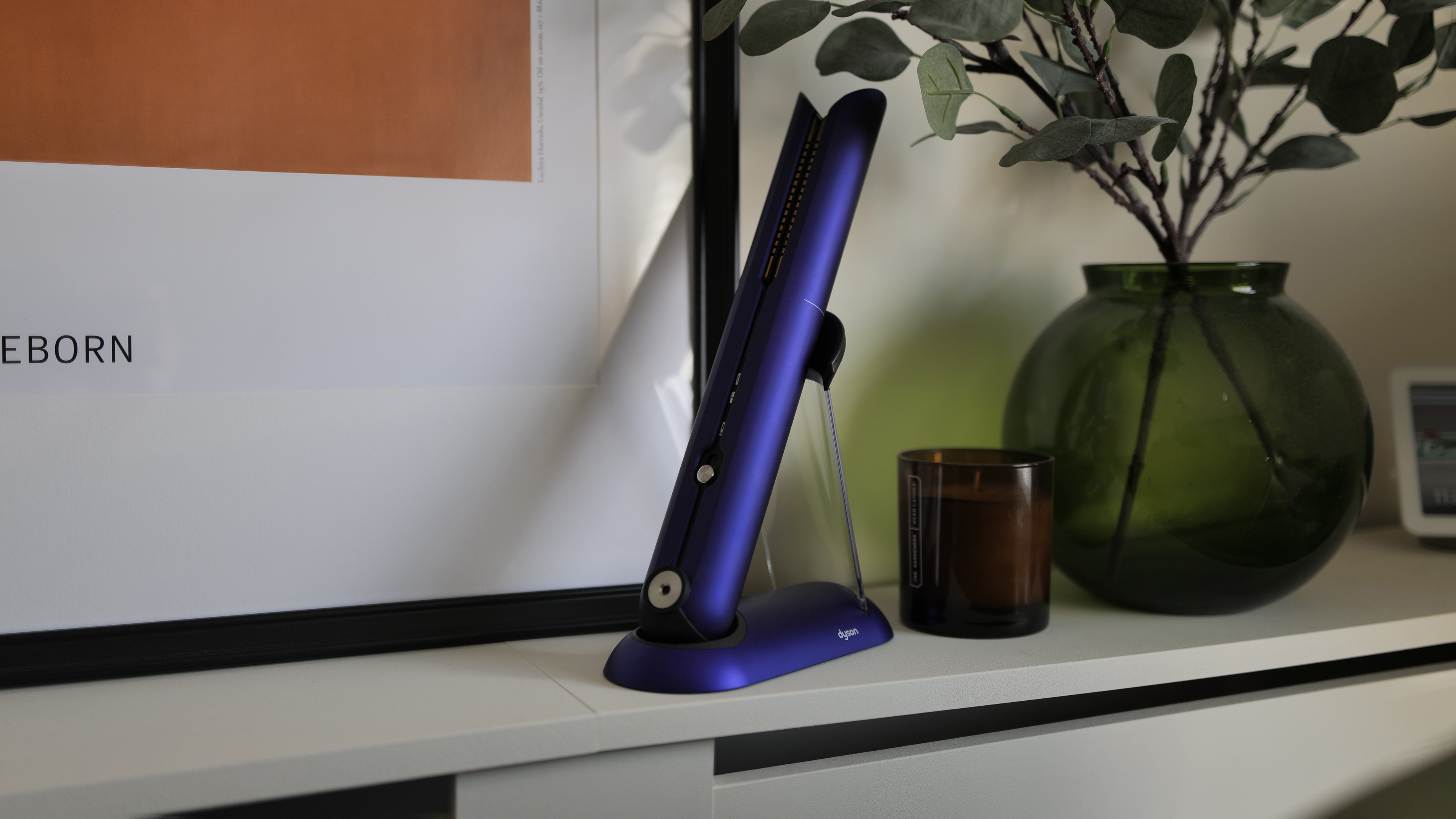 The Dyson Corale, one of the best hair straighteners, on a shelf next to. a candle and vase of leaves