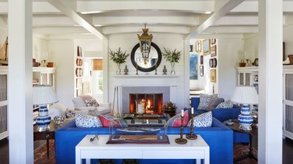 beamed living room with fire lit, blue sofas red and blue patterned cushions and boat pictures